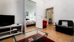 A modern living room with a flat-screen TV, a glass coffee table, a red chair, a black sofa, and a dining area with a small table and chairs. - Nagy Diofa 18 Apartment I. (Budapest)