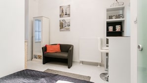 A modern bedroom with a bed, a dark sofa, a radiator, and a shelf with decorative items. - Nagy Diofa 18 Apartment II. (Budapest)