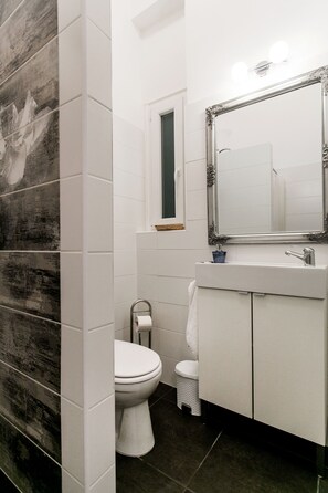 A bathroom with a white toilet, a sink with a mirror above it, and a window above the toilet. - Nagy Diofa 18 Apartment II. (Budapest)