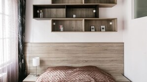 A hotel room with a wooden headboard, a bed with a patterned bedspread, and a wall-mounted shelf unit with various items. - Nagymezo 33 Apartment (Budapest)