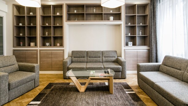 A modern living room with a grey sofa, a glass coffee table, and built-in wooden shelving with decorative items. - Nagymezo 33 Apartment (Budapest)