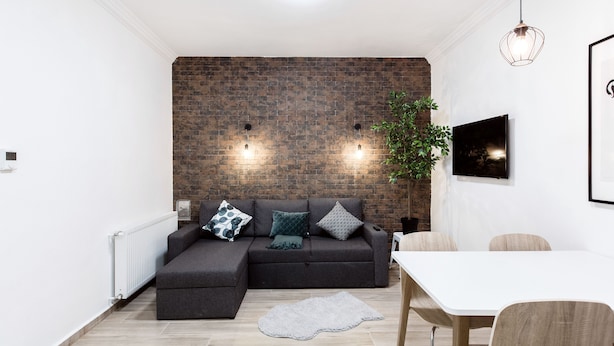 A modern living room with a sectional sofa, a white dining table, and a brick accent wall. - Nyar 7 Apartment (Budapest)
