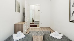 A hotel room with a wooden dresser, a mirror, a gray rug, and two gray sofas with towels. - Nyar 7 Apartment (Budapest)