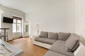 A modern living room with a white sofa, a flat-screen TV mounted on the wall, and a wooden floor. - O 40 Apartment (Budapest)