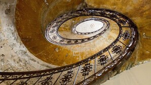A spiral staircase with ornate metal railings and a marble floor. - O 40 Apartment (Budapest)