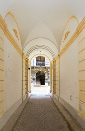 Un couloir orné d’arches, d’où l’on aperçoit un bâtiment doté d’un balcon.