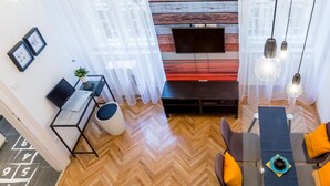 A modern living room with a wooden wall, a TV, a laptop on a desk, and a dining area with orange cushions. - Oktober 6 6 Apartment (Budapest)