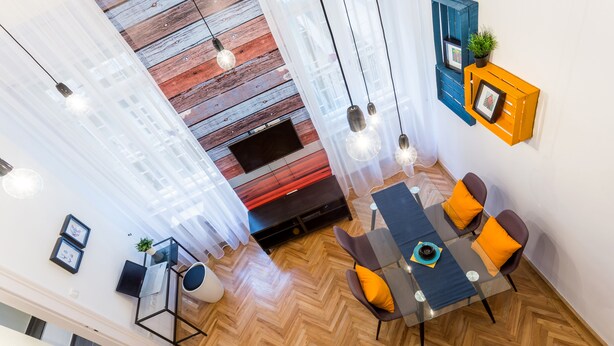 A modern living room with a herringbone wood floor, a glass coffee table, and orange cushions. There is a flat-screen TV mounted on the wall, a black sofa, and a small side table with a plant. - Oktober 6 6 Apartment (Budapest)