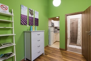 Una habitación con paredes verdes, un aparador blanco, una estantería con revistas y una puerta que da a una cocina.
