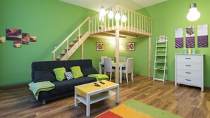 Una habitación con una cama individual doble, un sofá, una mesa de comedor con sillas y un aparador blanco.