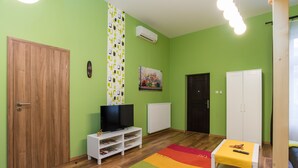 Una habitación con puerta de madera, un mueble blanco para televisor, un radiador, un armario blanco y una alfombra colorida.
