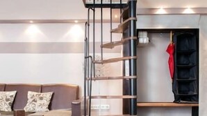 A modern living room with a wooden floor, a brown sofa, a green rug, and a spiral staircase. - Rakoczi 60 Apartment (Budapest)