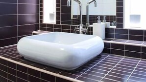 A modern bathroom with a large rectangular sink, dark tiled walls, and a large mirror above the sink. - Rakoczi 60 Apartment (Budapest)