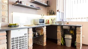 A kitchen with a microwave, stove, and various kitchen utensils on the counter. There are two shelves above the counter holding kitchen items. - Rakoczi 60 Apartment (Budapest)