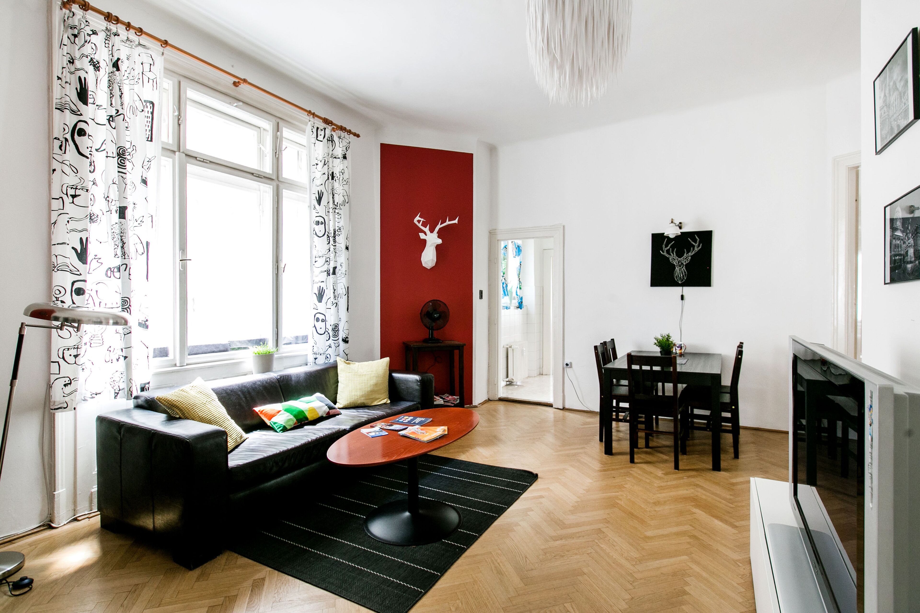 A modern living room with a black sofa, a wooden dining table, and a TV.