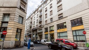 Vista de una calle con coches estacionados, una señal de prohibido el paso y un edificio con un letrero que dice 'KAPITAR'.