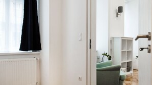Ein Zimmer mit Fischgrätparkett, einem Heizkörper, einem schwarzen Vorhang und einem grünen Sofa im Hintergrund.