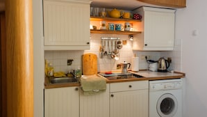Una cocina con armarios blancos, una encimera de madera, una lavadora y diversos utensilios de cocina.