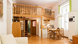 Un amplio espacio habitable con una escalera de madera que sube a un nivel superior, un comedor con sillas de madera y una cocina con armarios blancos.