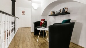 Un salon moderne avec un plancher en bois, un fauteuil noir, une table ronde blanche et une bibliothèque adossée au mur.