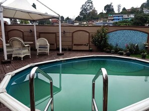 A swimming pool with a white deck and metal railings, surrounded by wicker chairs and a covered area with a white canopy. - Havelock Leisure (Ootacamund)
