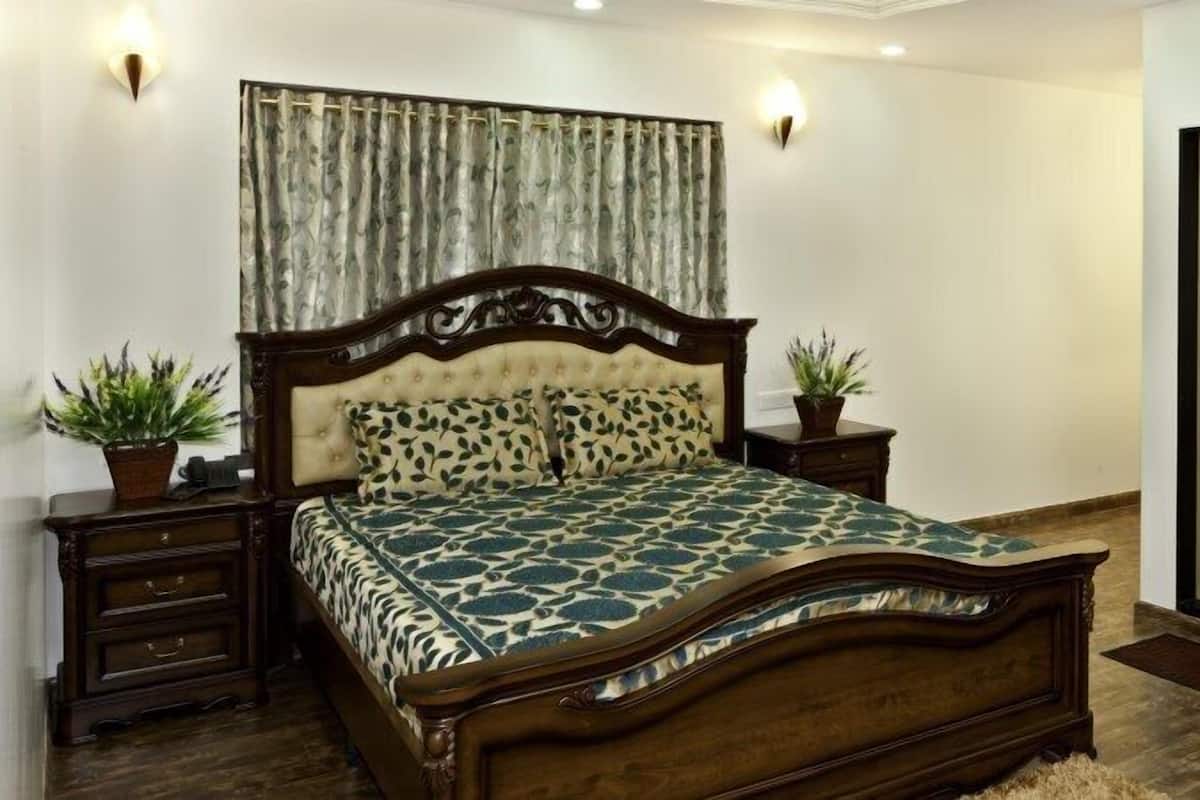 Un dormitorio con una cama de madera, dos mesitas de noche con plantas en macetas, un aparador y un espejo grande.