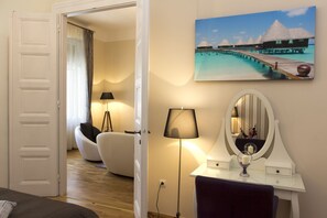 Habitación de hotel con una cama, un escritorio con espejo, una lámpara y un cuadro de una playa tropical.