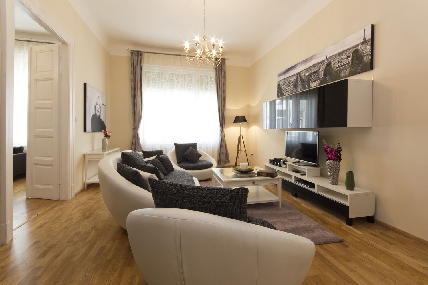 A modern living room with a sofa, armchairs, a coffee table, a TV, and a painting of a cityscape.