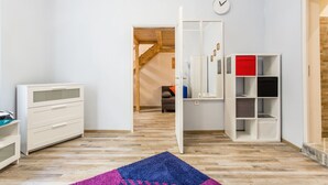 A room with a wooden floor, white walls, a blue and pink rug, a white dresser, a white cabinet, and a red storage unit. - Vorosmarty 73 Apartment (Budapest)