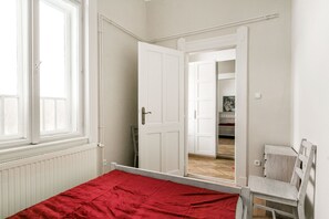 A bedroom with a bed, a chair, a wardrobe, and a door leading to a hallway.