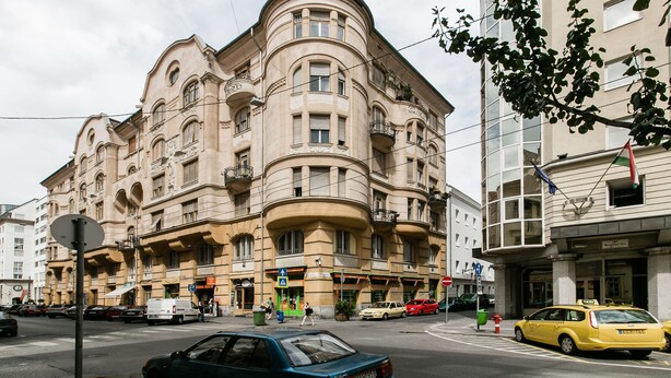 Un edificio histórico de varios pisos y balcones, situado en una esquina con coches y un taxi.
