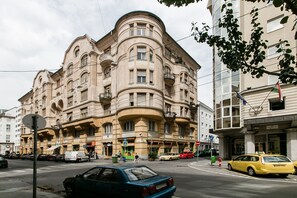 Un edificio histórico de varios pisos y balcones, situado en una esquina con coches y un taxi.