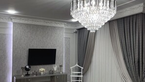 A room with a chandelier, a flat-screen TV, a dresser, and a ladder. - Art Apart Hotel (Tashkent)
