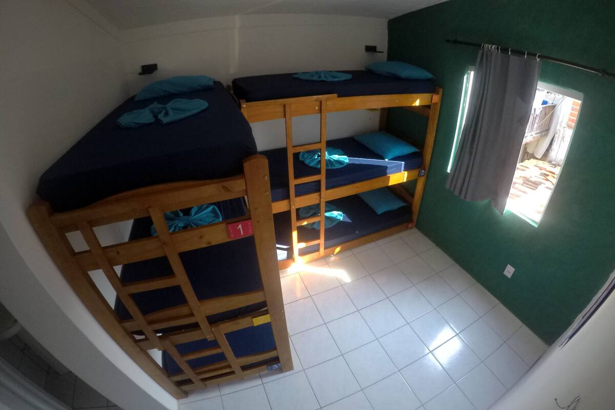A dormitory room with bunk beds, a window with curtains, and a tiled floor.
