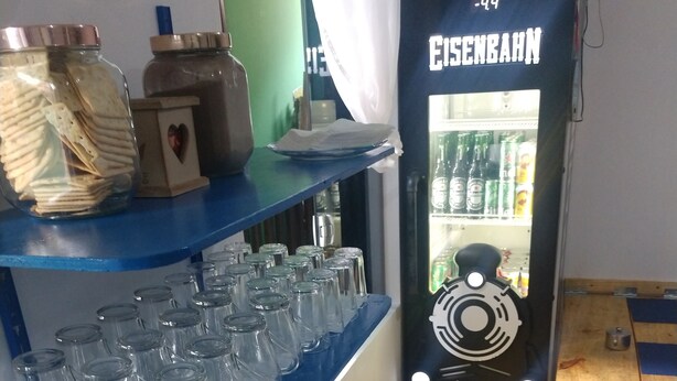 Keittiö, jossa on siniset työtasot, lasipurkkeja ja jääkaappi, jonka kylkeen on kirjoitettu teksti ”Eisenbahn”.