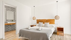 A modern bedroom with a wooden headboard, a large bed with white linens, two bedside tables, and a hanging light fixture.