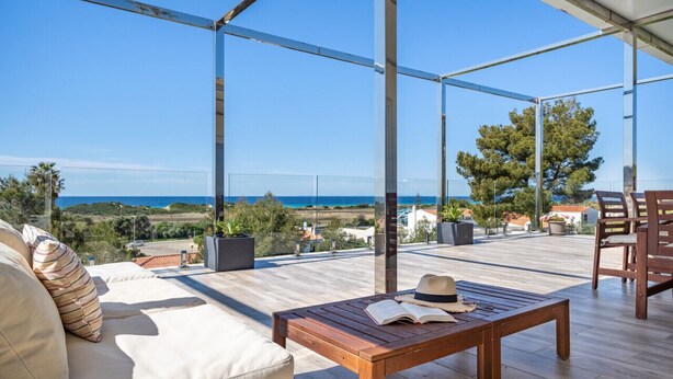 An outdoor patio with a wooden table, a sofa, and a view of the sea.