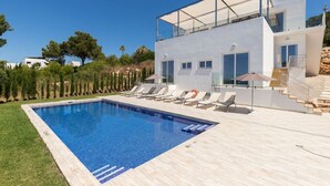 A modern villa with a swimming pool, sun loungers, and a glass-roofed terrace.