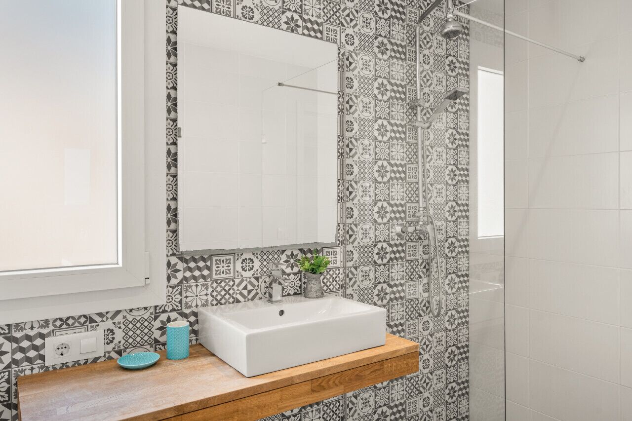 Un baño con baldosas estampadas, un lavamanos blanco, un espejo y una ducha.