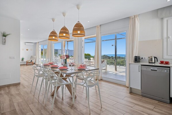 A modern dining area with a large table, white chairs, and pendant lighting.