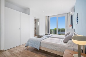 Ein Schlafzimmer mit zwei Betten, einem Kleiderschrank, einem Nachttisch mit Lampe und Blick ins Freie.