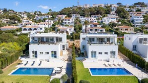 En modern villa med pool, omgiven av frodig grönska och belägen på en sluttning med liknande fastigheter.