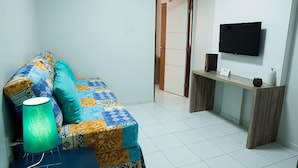 Une petite pièce, bien rangée, avec un canapé, un bureau et un téléviseur à écran plat.