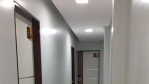 Un couloir aux murs blancs, doté d’un sol carrelé et de portes composées de panneaux de verre et de bois.