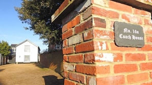 Un muro de ladrillo con un letrero que dice "No. 16a Coach House" y un edificio blanco al fondo.