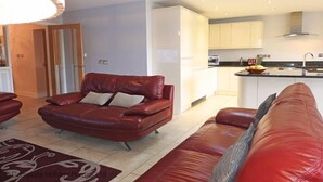 Una sala de estar moderna con un sofá de cuero rojo y una zona de cocina con armarios blancos y una isla central.