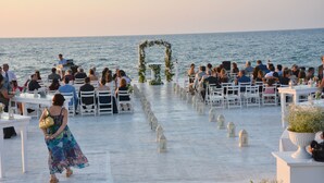A wedding ceremony on a boat with guests seated at tables, a floral arch, and lanterns on the deck.
