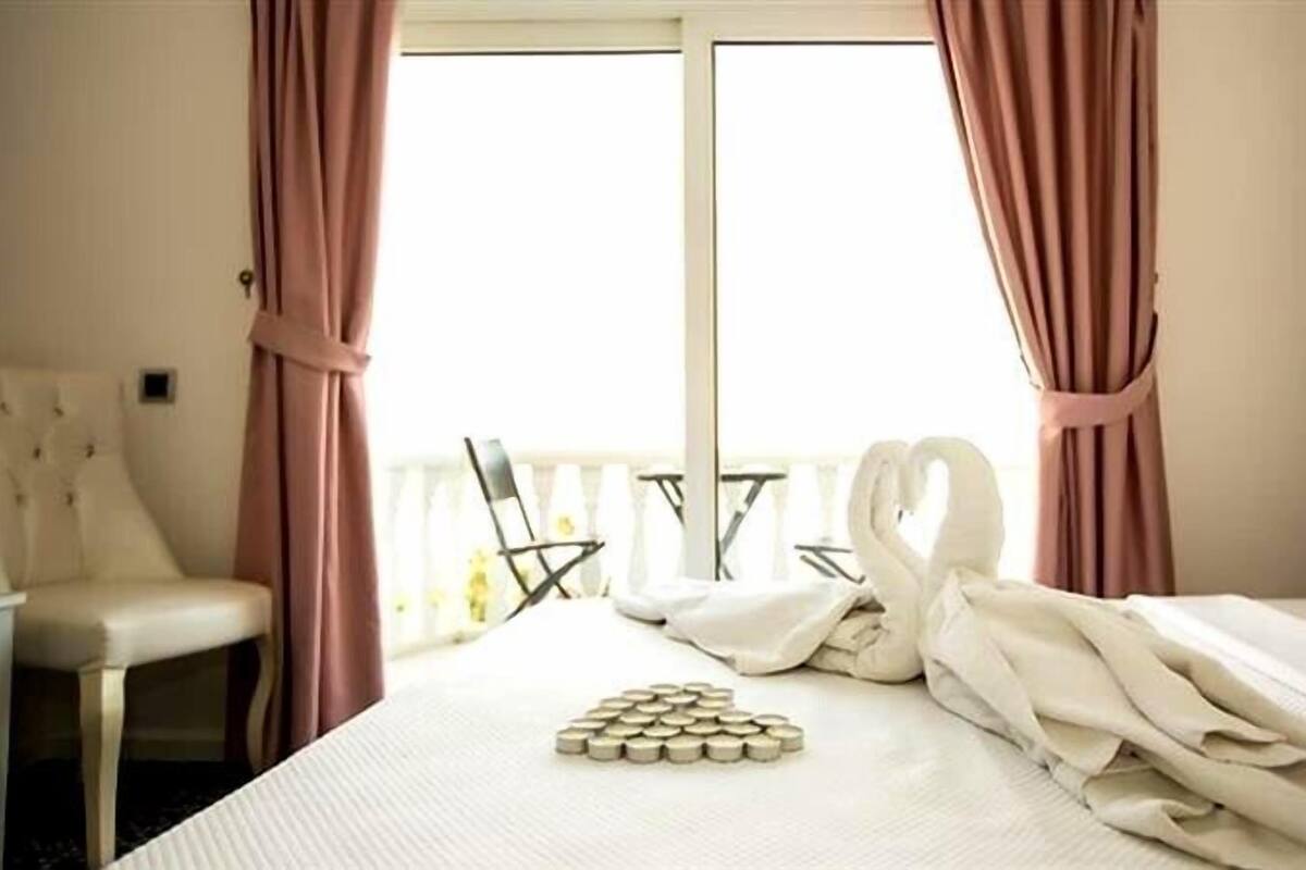A hotel room with a bed, a chair, a table, and a window with curtains.