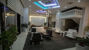 A spacious lobby with a modern design, featuring a seating area with sofas and chairs, a staircase, and a reception desk.