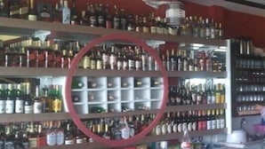 Eine Bar mit mehreren Regalen voller Spirituosenflaschen, einem runden Dekorationsobjekt und roten, gepolsterten Barhocker.